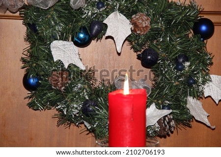 A burning red candle on the background of a Christmas wreath