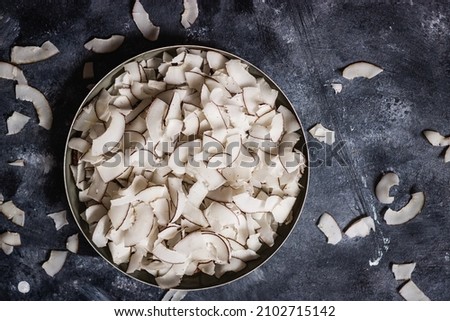 healthy snack: home made roasted coconuts chips in black bowl on dark background. Vegan. Clean eating. Plant based. Royalty-Free Stock Photo #2102715142