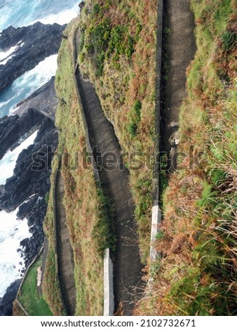 winding road leading down to the ocean, waves crashing against rocks in the background, green road Ponta Delgada Azores Portugal October 2021