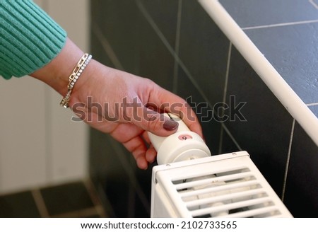 Close up shot of female's hand adjusting radiator temperature using thermostat. Home with central control heating.