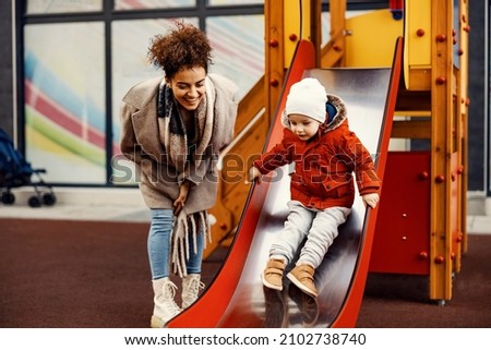 A nanny babysitting a little boy at the playground. A woman encourages a little boy on the slides. Royalty-Free Stock Photo #2102738740