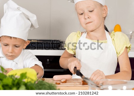 Little girl in a cooks uniform cutting ingredients for homemade pizza using a large knife to chop spicy sausages
