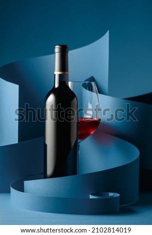 Bottle and glass of red wine on a blue background.