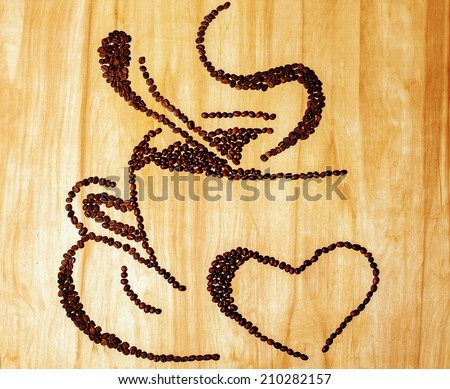 Coffee beans cup concept. Imbue beans of black coffee make a form of a cup with a spoon and ferry over wooden texture background. Studio shot. Copy space.