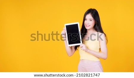 Asian employee woman showing screen tablet with blank monitor over isolated. Cheerful asia student girl holding digital tablet with smile on face on yellow background. Technology digital concept.