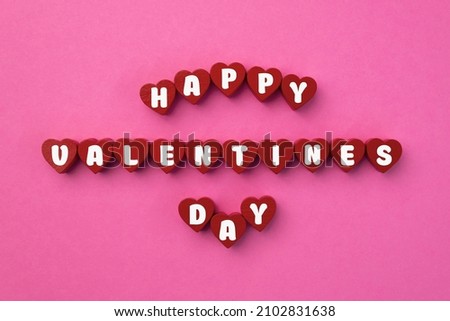 Red wood hearts with Valentine's day text on pink background. Love on wooden cubes. Theme of love. Valentine's day. Wooden blocks with the word love. Positive emotion. Copy space.