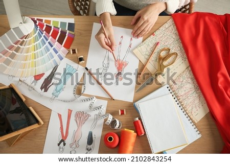 Fashion designer creating new clothes in sketchbook at wooden table, top view