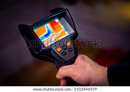 Professional thermal imaging camera in a man's hand. Inspection of the object for heat leaks.