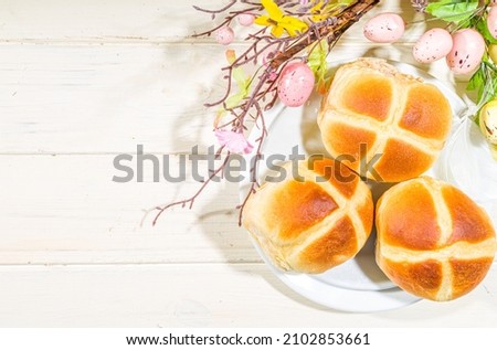 Traditional spring holiday Easter baking pastry – hot cross buns. On light wooden background with sunlight, Easter eggs, decor and spring branches