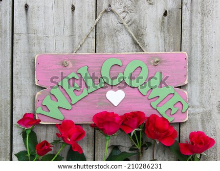 Pink weathered welcome sign with heart hanging on door with flower border of red roses