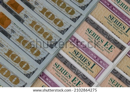 US Savings Bonds and 100 Dollar bills, representing investment choices. Savings bonds are debt securities issued by the U.S. Department of the Treasury and issued in Series EE or Series I. Royalty-Free Stock Photo #2102864275