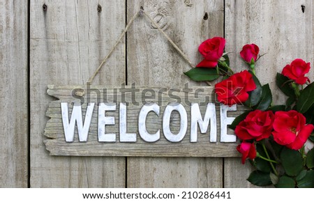 Rustic wooden welcome sign hanging on wood door with flower border of red roses