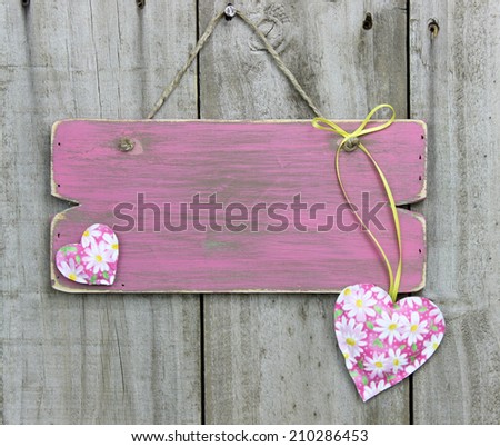 Blank weathered pink sign with flower hearts hanging on wooden door