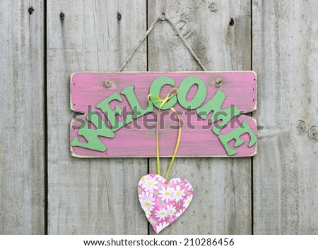 Weathered pink welcome sign with flower hearts hanging on wooden door