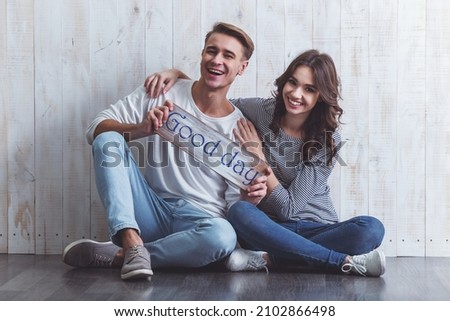 Happy young couple keeping the sign that says, sitting on the floor Wooden at home