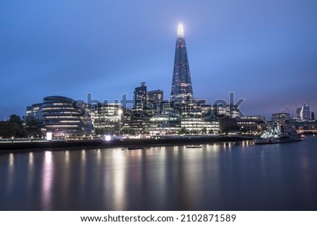 London skyline, lit up at night, with the lights reflecting on the smooth water of the river Thames