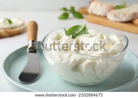 Tasty cream cheese with basil and knife on white wooden table Royalty-Free Stock Photo #2102884675