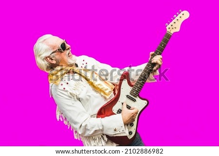 Senior bearded man playing guitar on coloured background - Elderly man playing rock n'roll music - Elderly, positive concept Royalty-Free Stock Photo #2102886982
