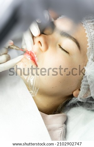 Young woman during professional permanent makeup procedure - lip blushing Royalty-Free Stock Photo #2102902747