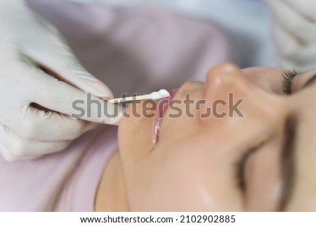 Professional permanent makeup artist applying anesthetic on client's lips before lip blushing procedure Royalty-Free Stock Photo #2102902885