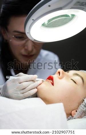 Professional permanent makeup artist and her client during lip blushing procedure Royalty-Free Stock Photo #2102907751
