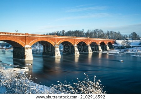 Vault Brick Bridge (built in 1874) over the Venta - one of the longest of its kind in Europe. Snowy winter morning in Latvia. Kuldiga. Architectural monument. Tourism. Royalty-Free Stock Photo #2102916592