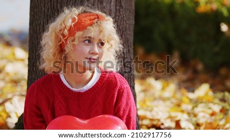 Thoughtful millenial blond girl sitting under the tree in autumn park - portrait. High quality photo