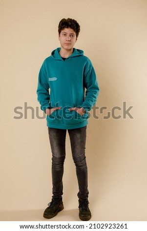 Dark hair handsome young boy in black t-shirt and green sweatshirt and black jeans stands and posing indoor  Royalty-Free Stock Photo #2102923261