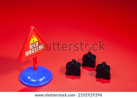 Black wooden human figures and a road sign for human attention on a red background.