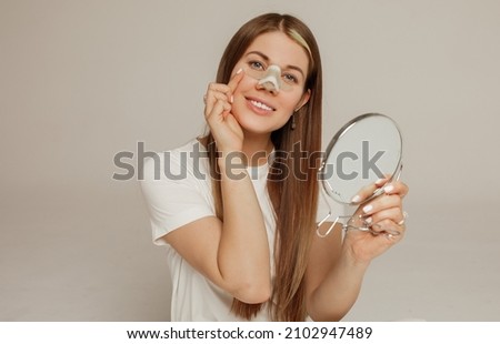 A young beautiful woman with a bandage on her nose after rhinoplasty with a mirror smiles Royalty-Free Stock Photo #2102947489