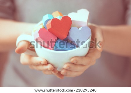 Bright paper hearts in mug in woman hands. Toned picture