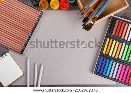 Blank sheet of paper, colorful chalk pastels and other drawing tools on wooden table, flat lay. Modern artist's workplace