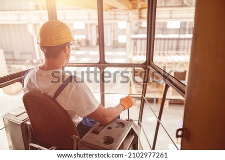 Male worker sitting in operator cabin of overhead crane Royalty-Free Stock Photo #2102977261