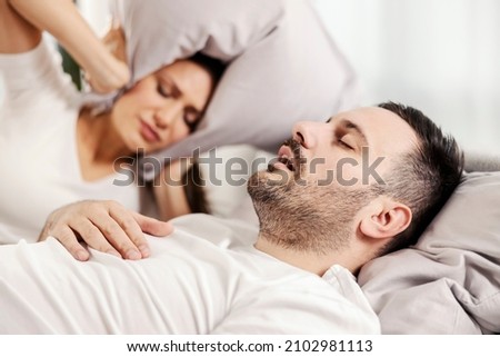 A man snoring and sleeping in the bed while woman is annoyed of it. Royalty-Free Stock Photo #2102981113