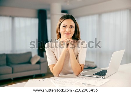 A happy woman finishing paperwork and home finances and smiling at the camera. Royalty-Free Stock Photo #2102985436