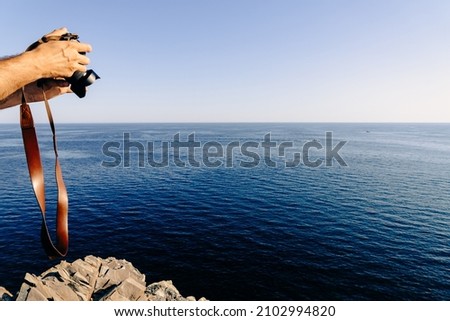 Hands of a man holding a camera filming a seascape on a cliff over the sea