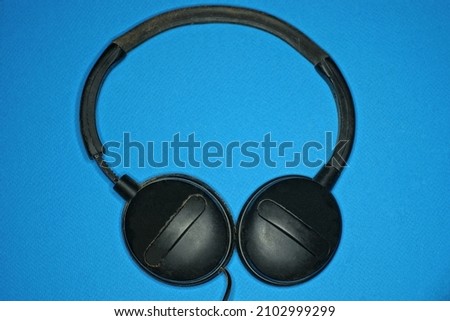 one big black audio headphones lies on a blue 