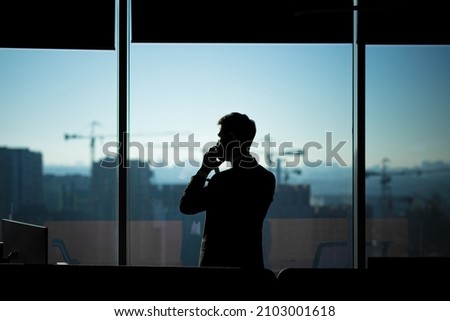 Silhouette of a businessman man in a modern office on the background of the window, a man talking on the phone Royalty-Free Stock Photo #2103001618