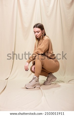 Young model woman in knitted suit, beige leather boots and sweater posing indoors