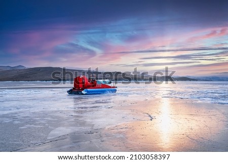 Colorful sunlight outside the mountain peaks is reflected on the ice of frozen Lake Baikal at sunset, winter landscape, cold feeling.