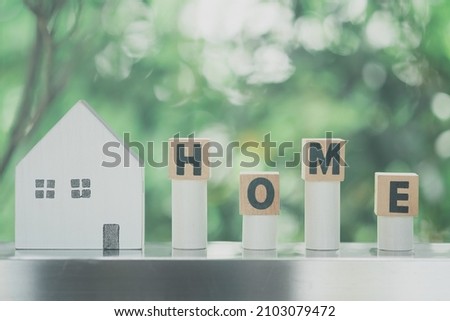 Text HOME on wood blocks and wood home on nature background. Conceptual image of first home and saving for buy home.