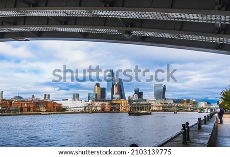 View of downtown London, England, from under the bridge  on nice day; Thames River in foreground; sky with light clouds in background