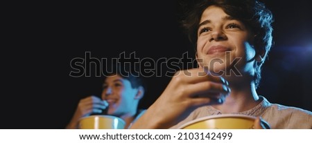 Boy watching a comedy movie at the cinema, he is eating popcorn and smiling Royalty-Free Stock Photo #2103142499