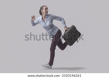 Scared businesswoman escaping from danger, she is running away and looking backwards, isolated on gray background Royalty-Free Stock Photo #2103146261