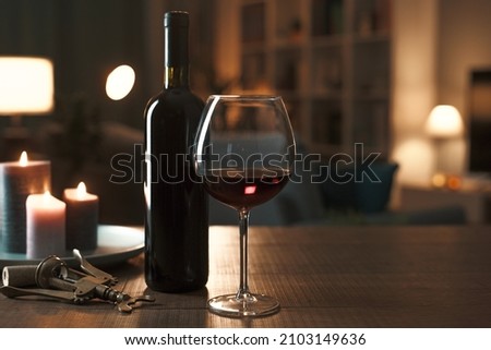 Red wine tasting at home: wine bottle, wineglass, corkscrew and candles on a table in the living room at night Royalty-Free Stock Photo #2103149636