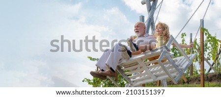 Old grandfather and young child grandson swinging in garden outdoors. Grand dad and grandson sitting on swing in park. Grandfather and grandchild, spring banner.