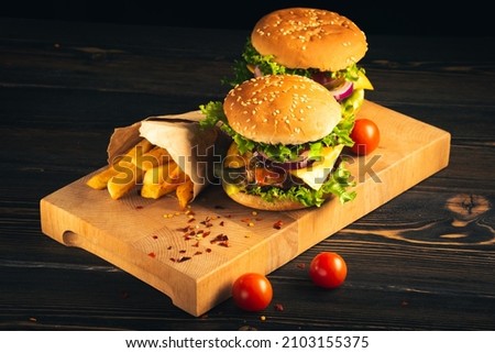 Tasty hamburgers on wooden board on dark background.
