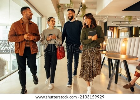 Young businesspeople walking through a modern office in the morning. Team of happy businesspeople smiling cheerfully. Group of diverse entrepreneurs working together in a co-working space. Royalty-Free Stock Photo #2103159929