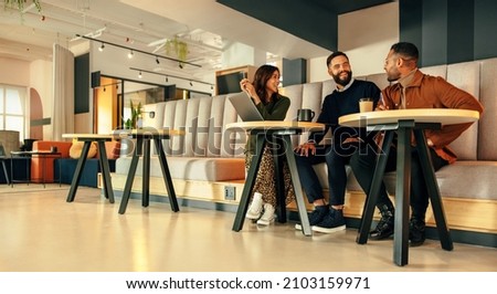 Three of businesspeople working in an office lobby. Team of happy businesspeople smiling while having a discussion. Group of modern entrepreneurs collaborating on a new project in a co-working space. Royalty-Free Stock Photo #2103159971