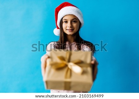 christmas, holidays and people concept - happy smiling teenage girl in santa helper hat holding gift box over lights on blue background